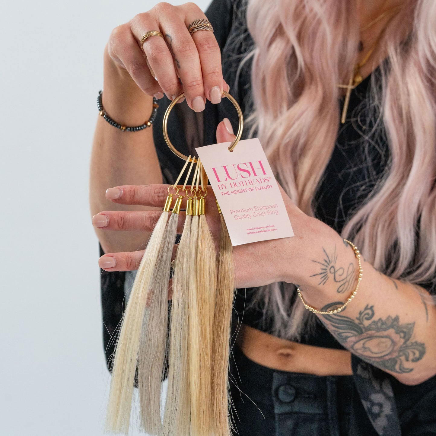 A woman is showcasing a pair of hair extensions from the Lush Color Ring collection, highlighting vibrant color options.