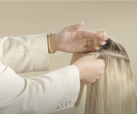 A hairdresser applying tape hair extensions to a woman.
