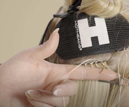 A woman carefully applies a weft hair extension sewing it in to enhance her hairstyle.