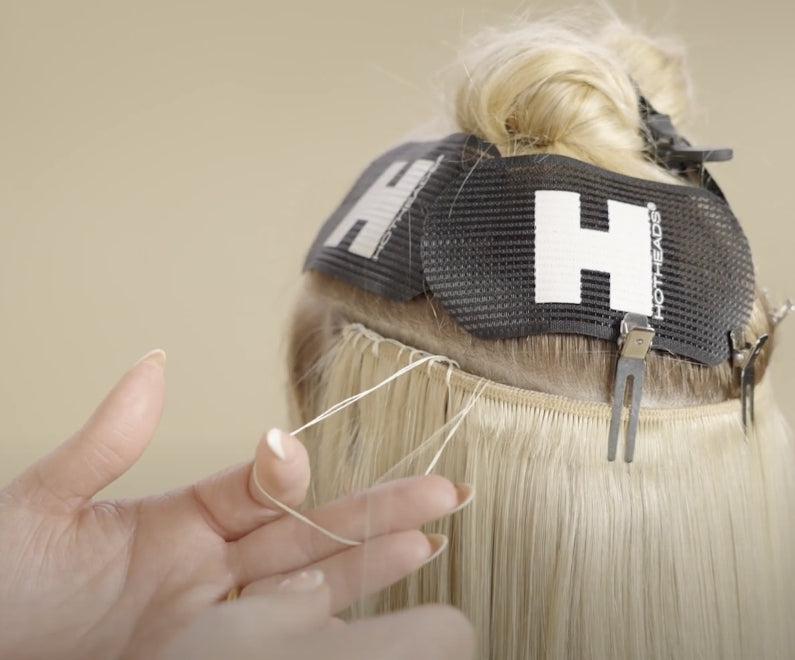 A woman is trimming the hair of a blonde woman, showcasing the process of applying a blanket stitch to hair extensions.