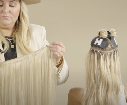A stylist holding a long blonde hair extension, preparing to attach it to a client's head.