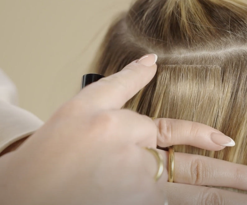 A woman's hand is showing the tape extension in hair, against her hair.