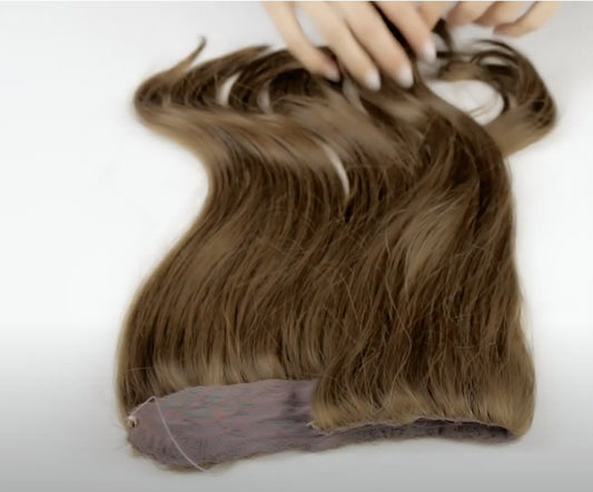 Brown hair extension with a lace band, shown lying flat on a surface, with hands positioned on the extension.